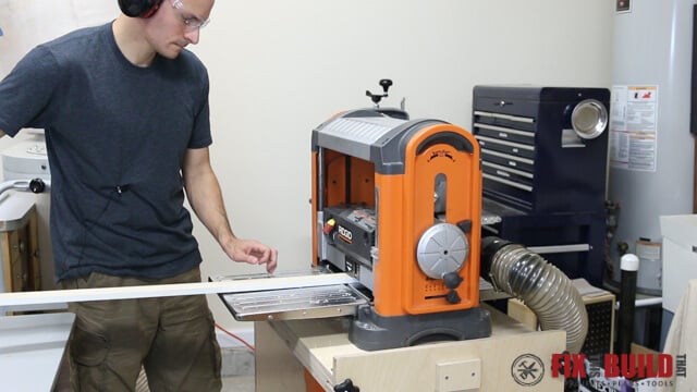 Manually lifting the end of a board slightly as it feeds into a RIDGID lunchbox planer to prevent the opposite end from tipping up into the cutter head and causing snipe
