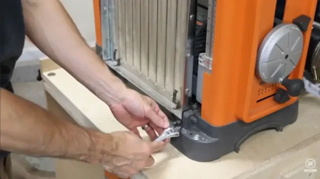 Adjusting the infeed table height on a RIDGID lunchbox planer using a wrench to access the set screw at the base of the folded table