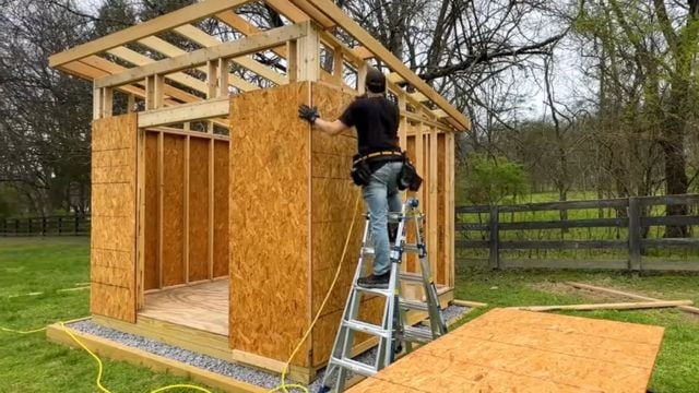 A man installs plywood sheathing on a 10x12 DIY Modern Shed.