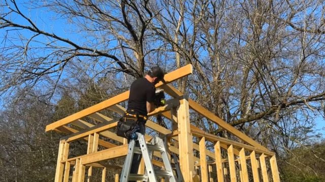 A man nails the roofing structure onto a 10x12 DIY Modern Shed.