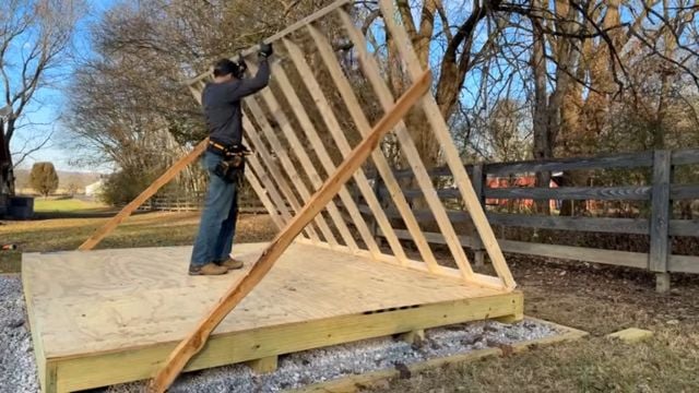 A man raises the first framed wall of a 10x12 DIY Modern Shed.