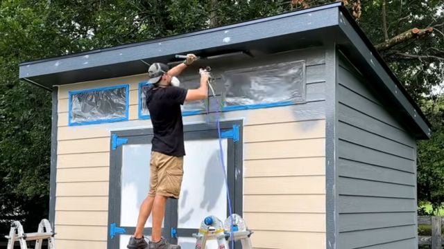 A man uses a paint sprayer to paint a 10x12 DIY Modern Shed.
