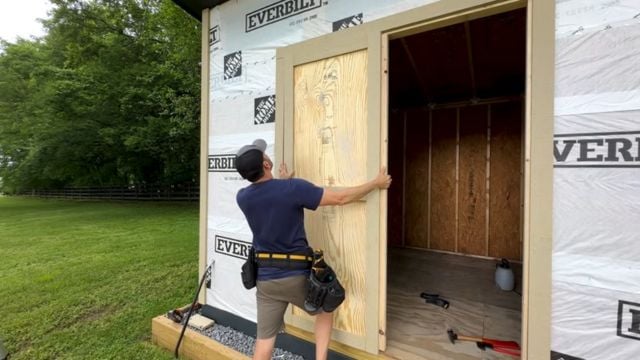 A man installs a custom door on a 10x12 DIY Modern Shed.