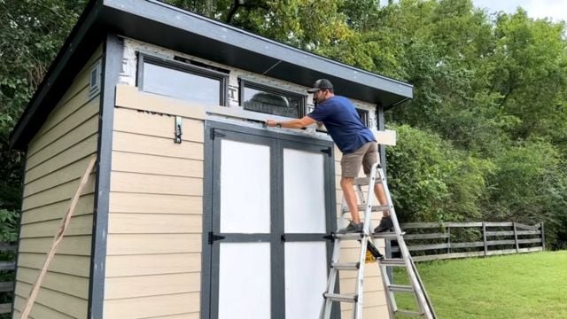 A man installs siding on a 10x12 DIY Modern Shed.